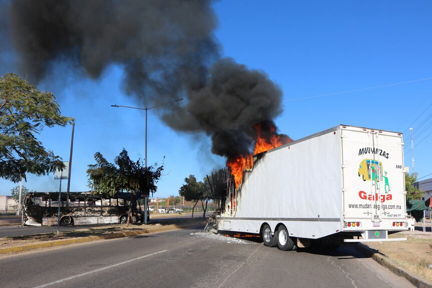 A burnt bus sits on a wide street as a truck burns alongside it in Culiacan, Mexico.