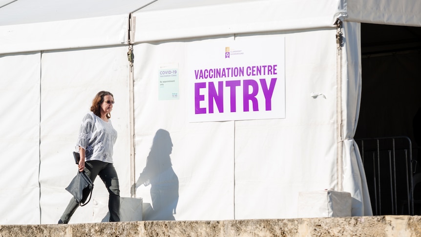 A woman walks past a tent with a sign reading "vaccination centre entry".