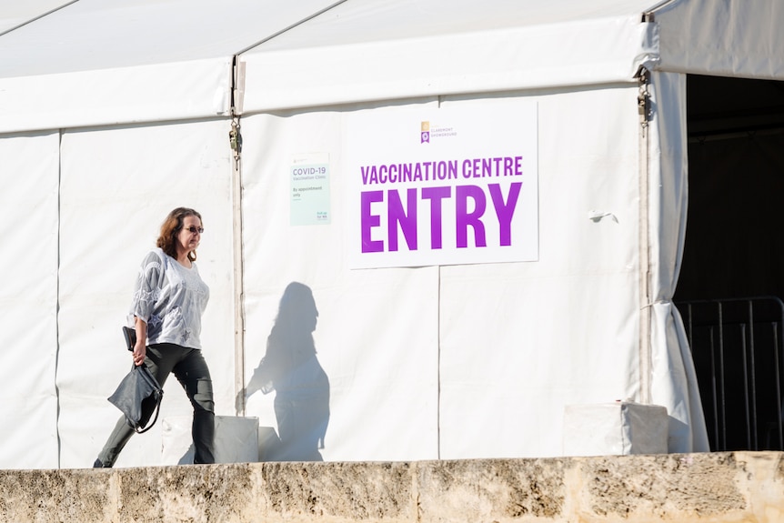 A woman walks past a tent with a sign reading "vaccination centre entry".