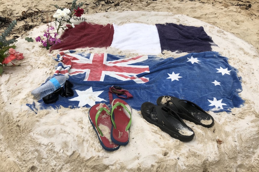 Two towels featuring the pattern of the French and Australian flags on a beach with thongs and keys.