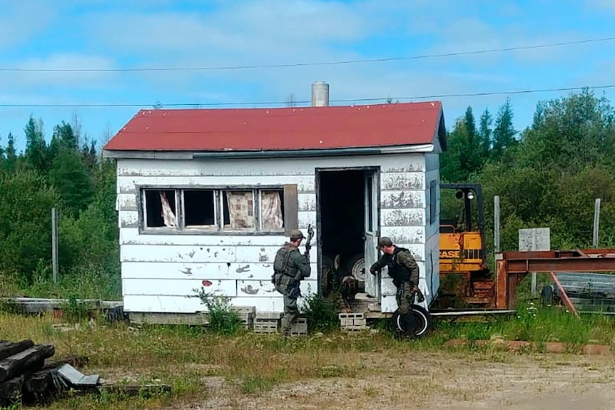 A pixelated image shows two camouflaged police officers entering a dilapidated white wooden shack with a red gable roof.