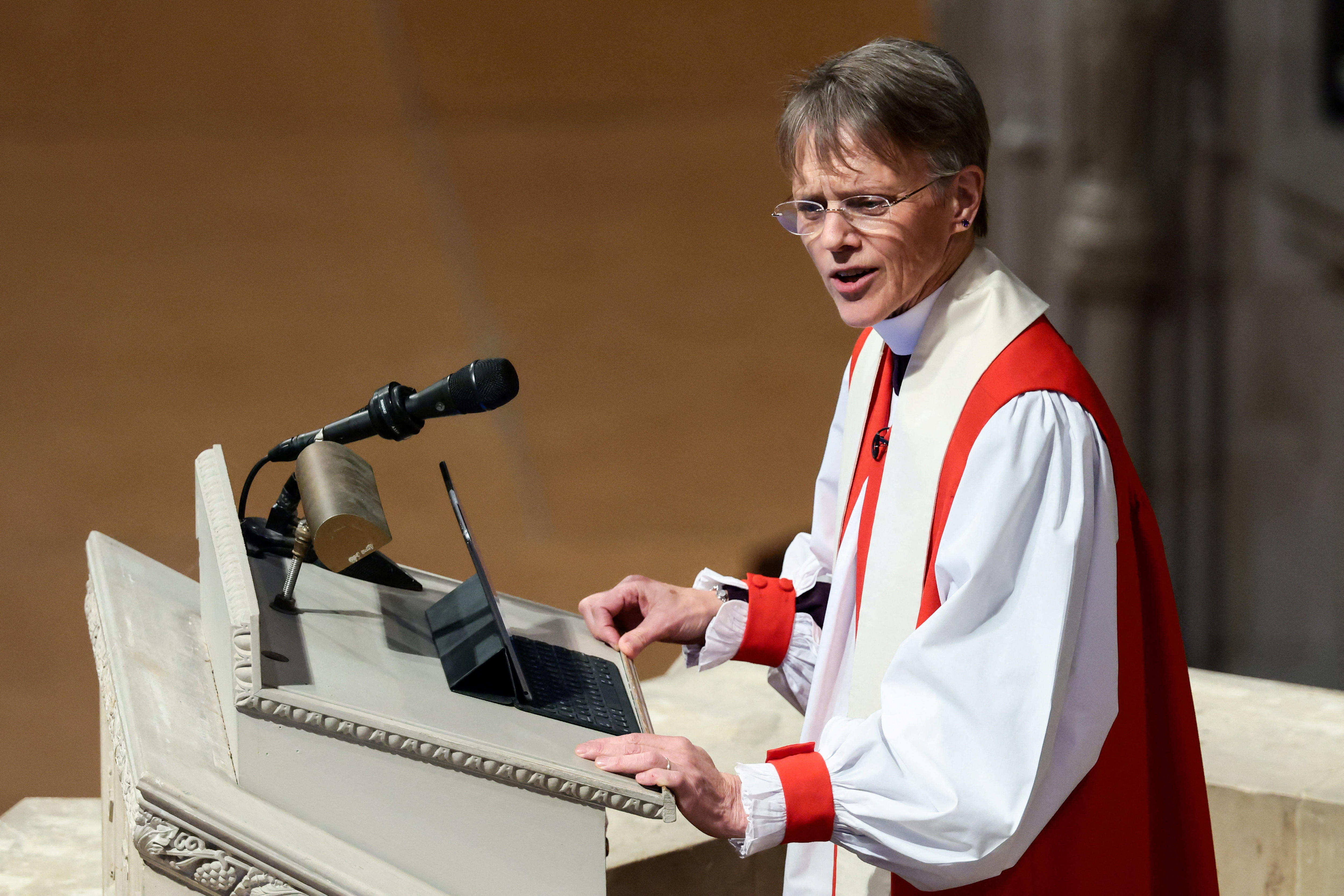 A female priest speaks at a stone lectern in a cathedral.
