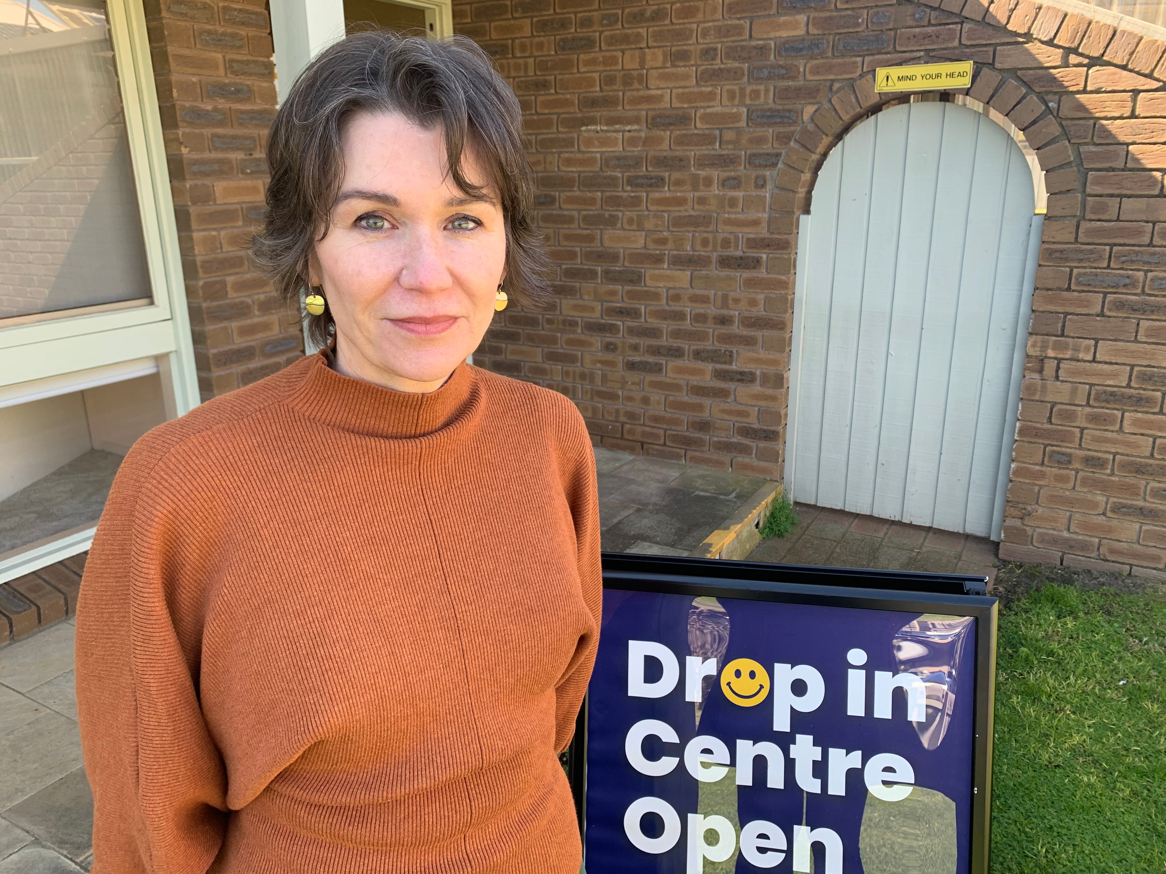 Anne-Marie Kaser stands in front of a house and a sign that says drop-in centre.