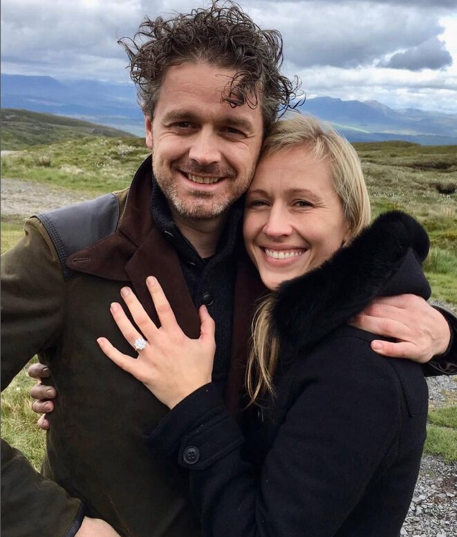 A woman wearing a wedding ring has her hand on a man's chest as he wraps his arms around her.