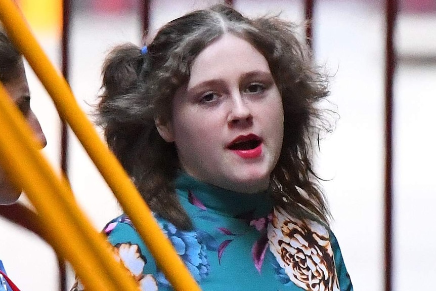 A young woman wearing pink lipstick and a colourful printed top looks towards the camera.