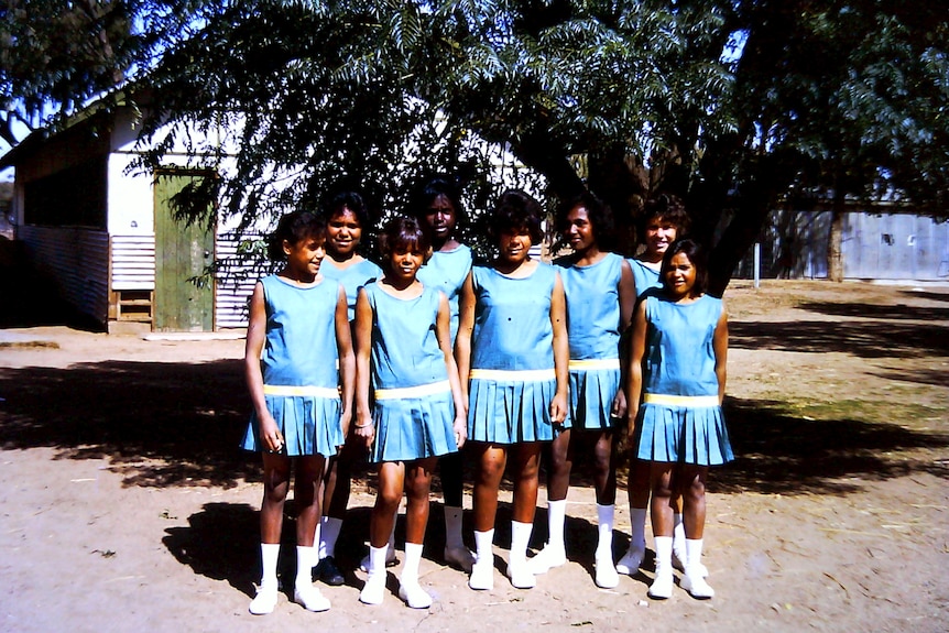 A group of girls wearing blue sports uniforms standing in a row.