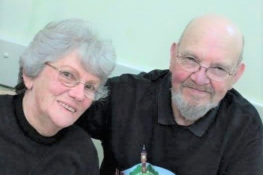 Close up frame of elderly couple, female and male, smiling at camera. Both wearing glasses. 