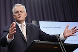 Scott Morrison speaks before a podium with outstretched arms, with a presentation beside him.