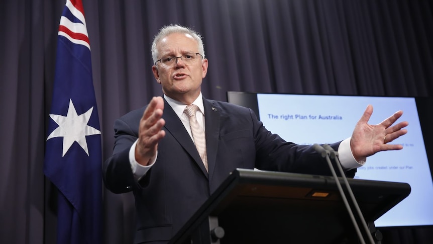 Scott Morrison speaks before a podium with outstretched arms, with a presentation beside him.