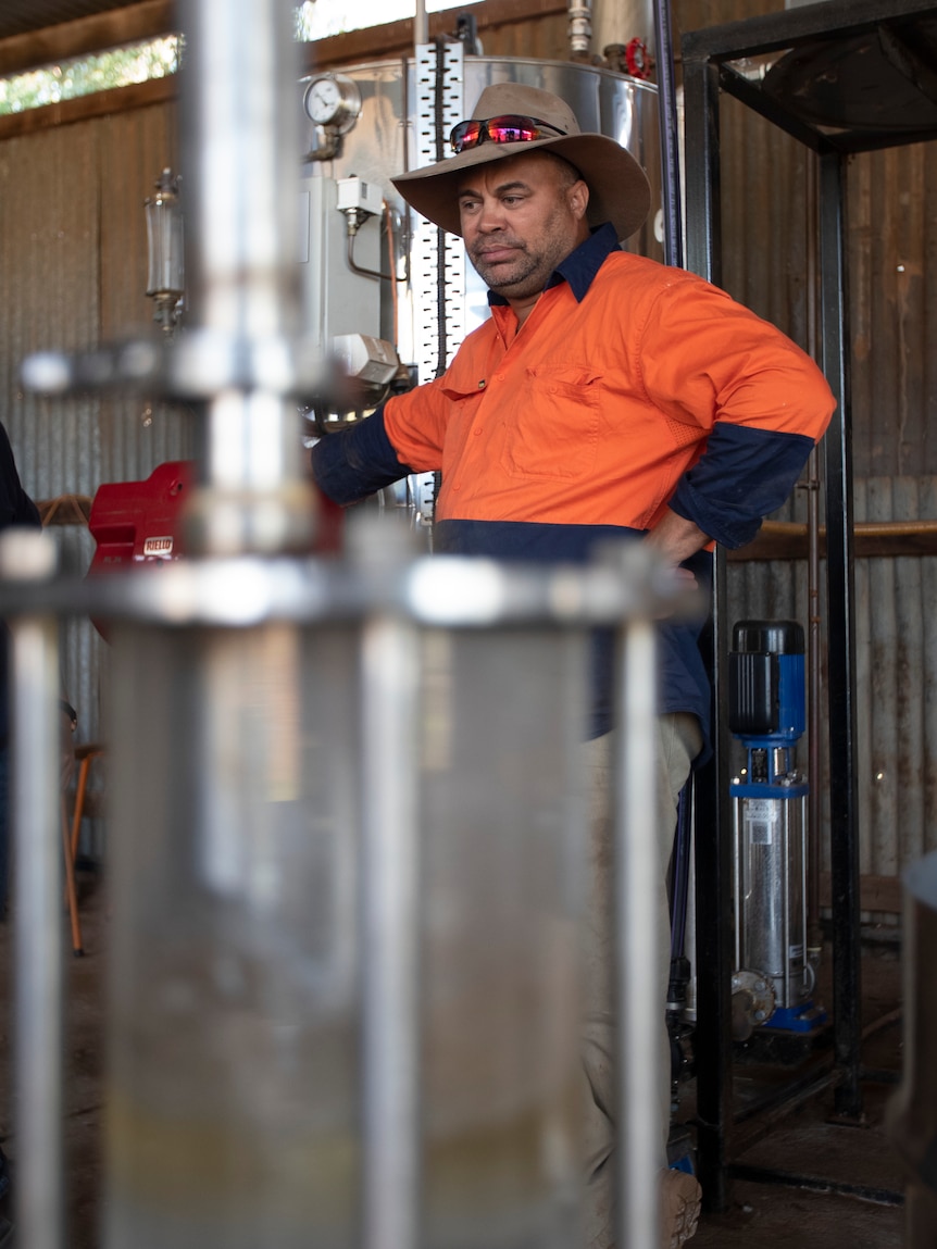 A man in orange high-vis stands behind a shiny metal machine.