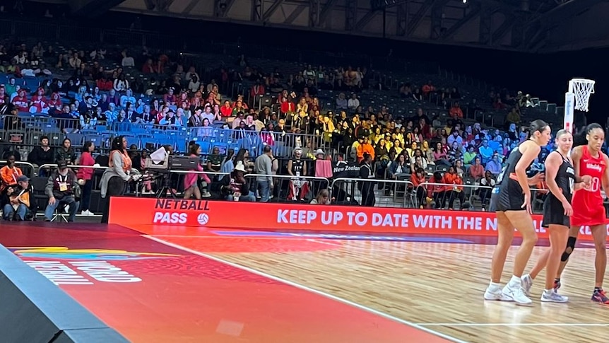A shot of players on the court at a Netball World Cup game, with the crowd behind them, including a section of empty seats.