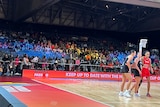 A shot of players on the court at a Netball World Cup game, with the crowd behind them, including a section of empty seats.