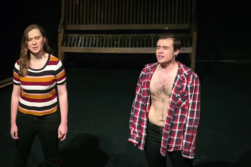 A trans man who has undergone top surgery has his shirt open on stage.