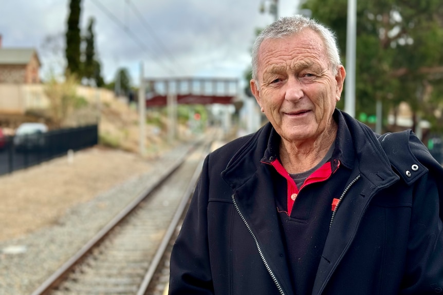 A man with black shirt and jacket stands by a railway line