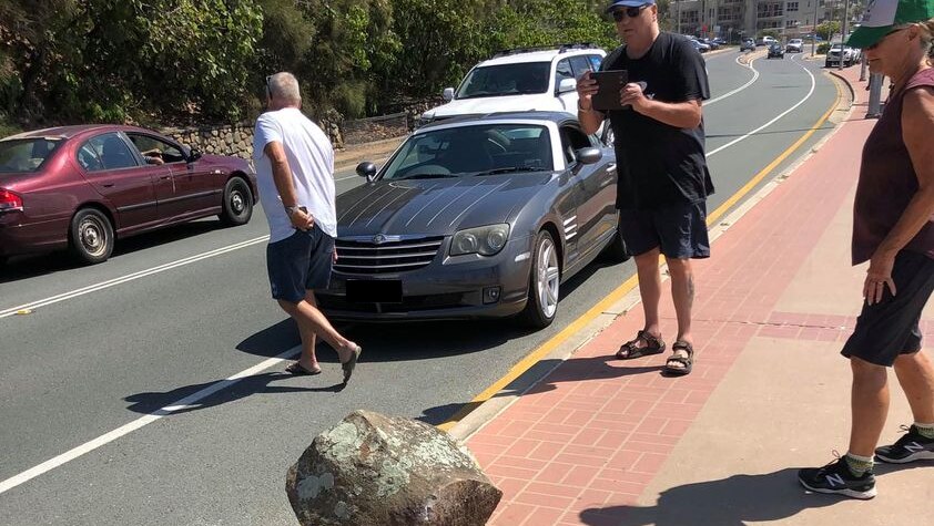 Men and women standing around a car and big boulder, taking photos.
