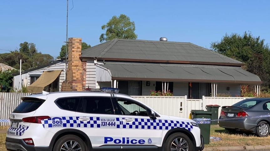 A police vehicle parked in front of a house with a grey tin roof, white weatherboard and white fencing. 