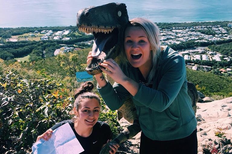 two women with the dinosaur on top of a mountain overlooking the ocean