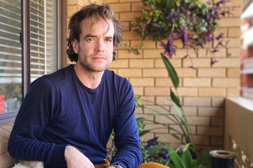Jonny Hawkins sits on a balcony of a flat, for a story about renting and the coronavirus.