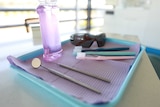 Dental instruments, toothbrushes, mouth wash and sunglasses on a tray.
