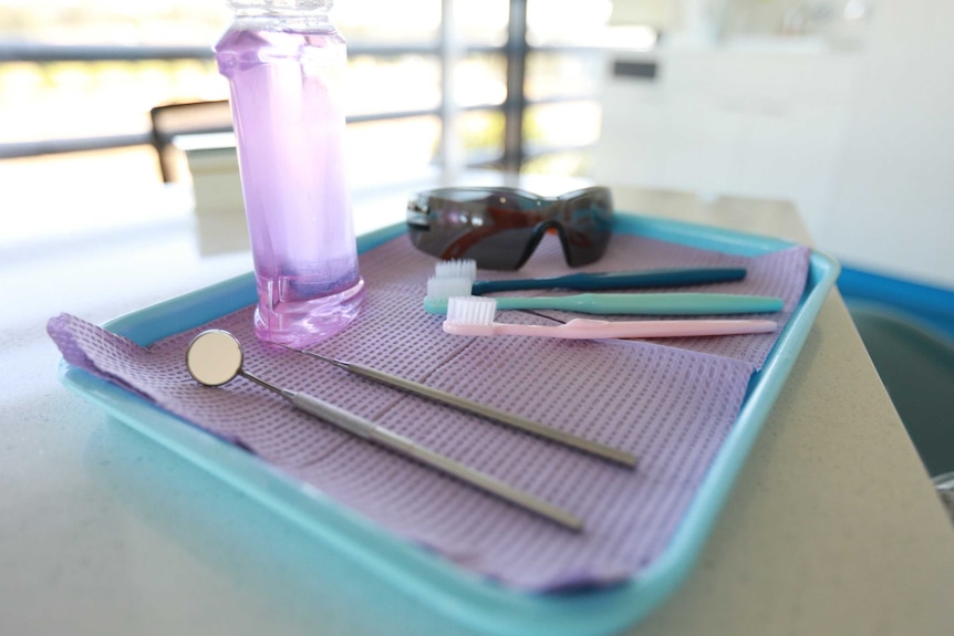 Dental instruments, toothbrushes, mouth wash and sunglasses on a tray.