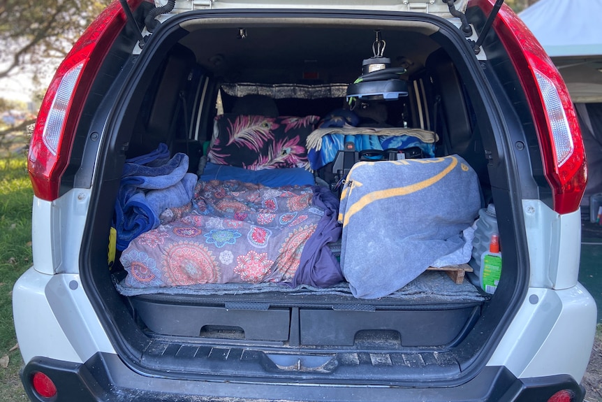 Back of a white car with boot open, revealing a bed.