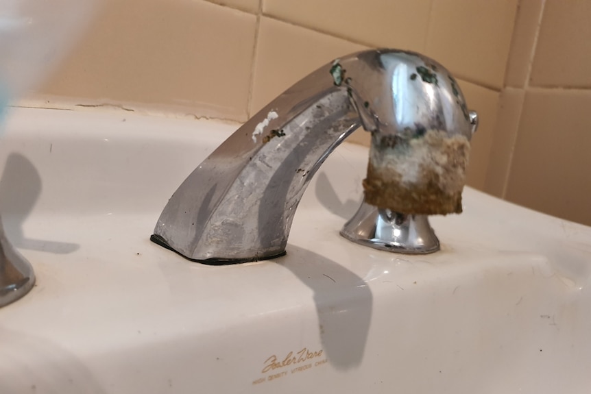A chrome tap with a rusty washer on a white bathroom basin.