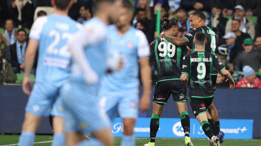 Melbourne City players are blurry in the foreground as Western United A-League players hug in the background.