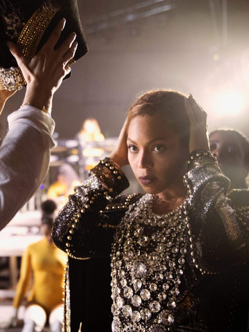 A bejewelled headdress is placed on Beyonce's head. She is wearing a diamonte dress