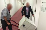 Two men deliver a safe to the ABC Parliament House Bureau, on a trolley. Their faces are blacked out for legal reasons.