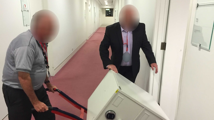 Two men deliver a safe to the ABC Parliament House Bureau, on a trolley. Their faces are blacked out for legal reasons.