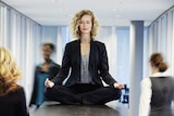 A woman meditates on an office desk.
