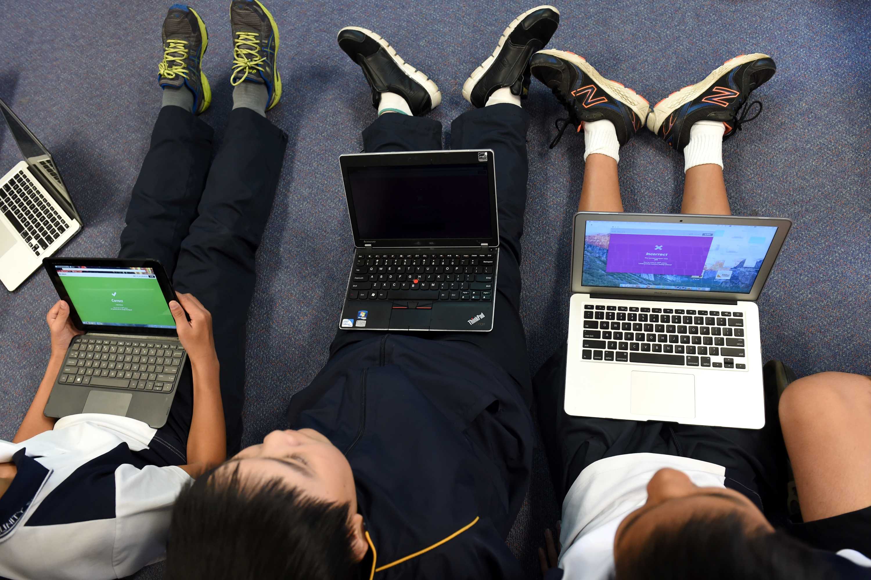 Three children sitting on the floor with laptop computers on their laps.