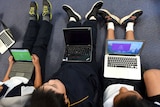 Three children sitting on the floor with laptop computers on their laps.