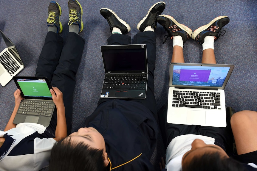Three children sitting on the floor with laptop computers on their laps.