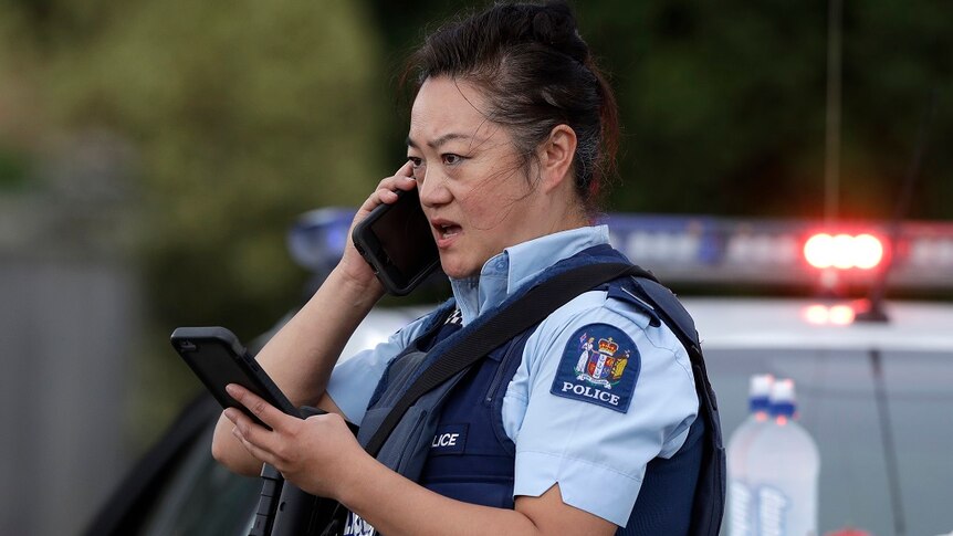 An armed female police officer speaks on a mobile phone while she looks at another mobile phone as she stands at a roadblock