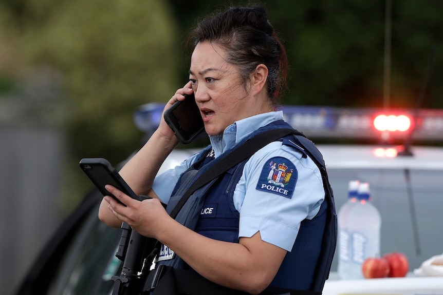 An armed female police officer speaks on a mobile phone while she looks at another mobile phone as she stands at a roadblock