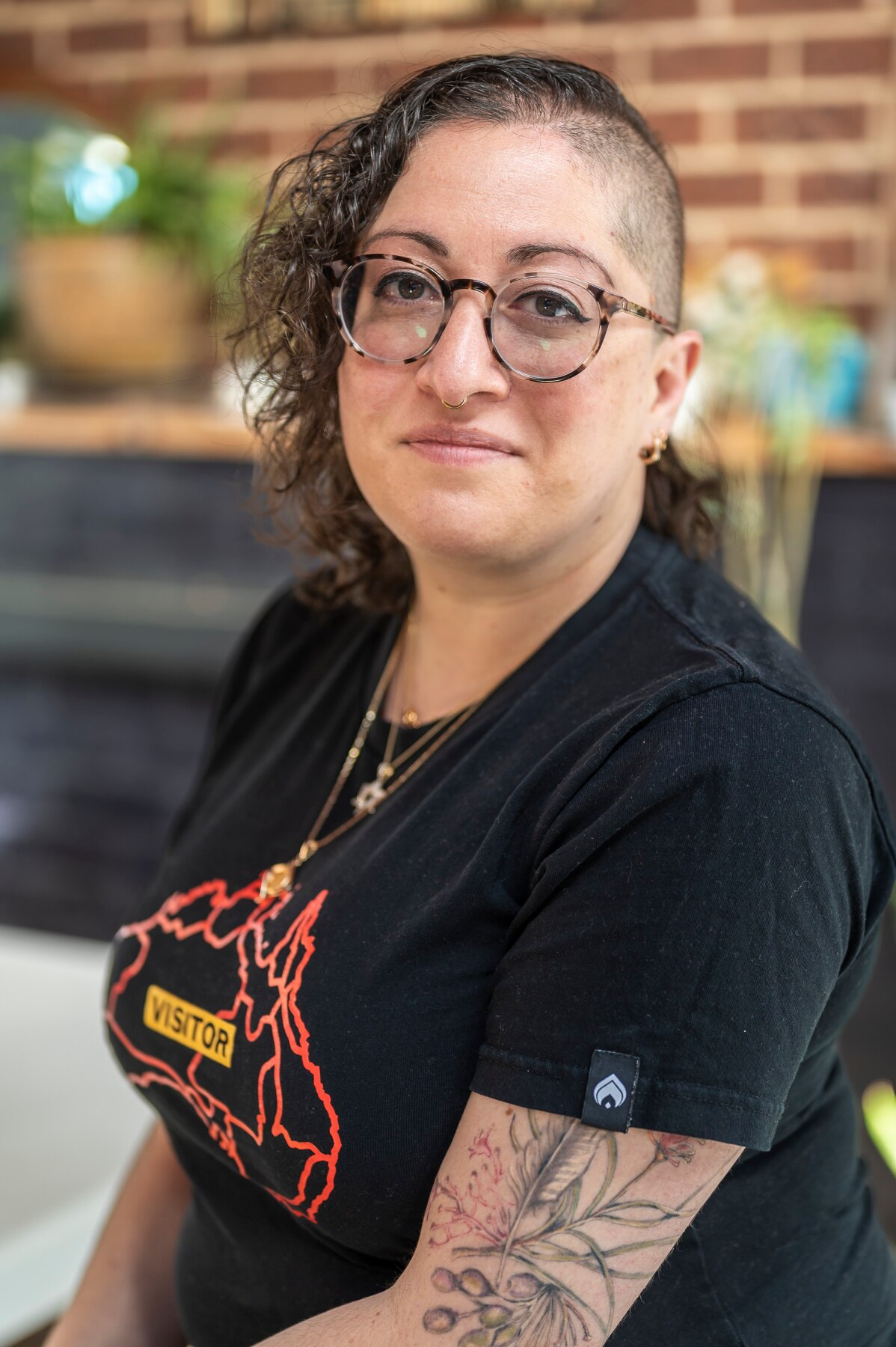 Isabelle Oderberg, with glasses, brown curly hair and half-shaved head, and black t-shirt, smiles with mouth closed.
