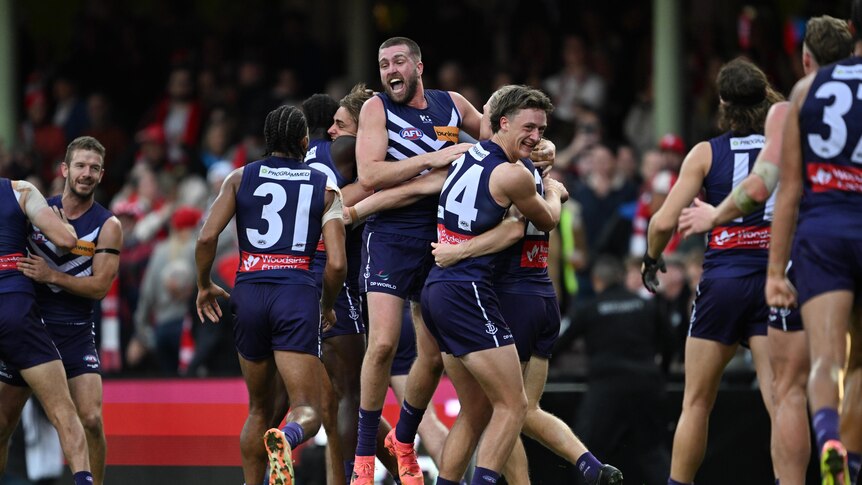 A group of Fremantle Dockers AFL players come together and embrace in celebration after a win. 
