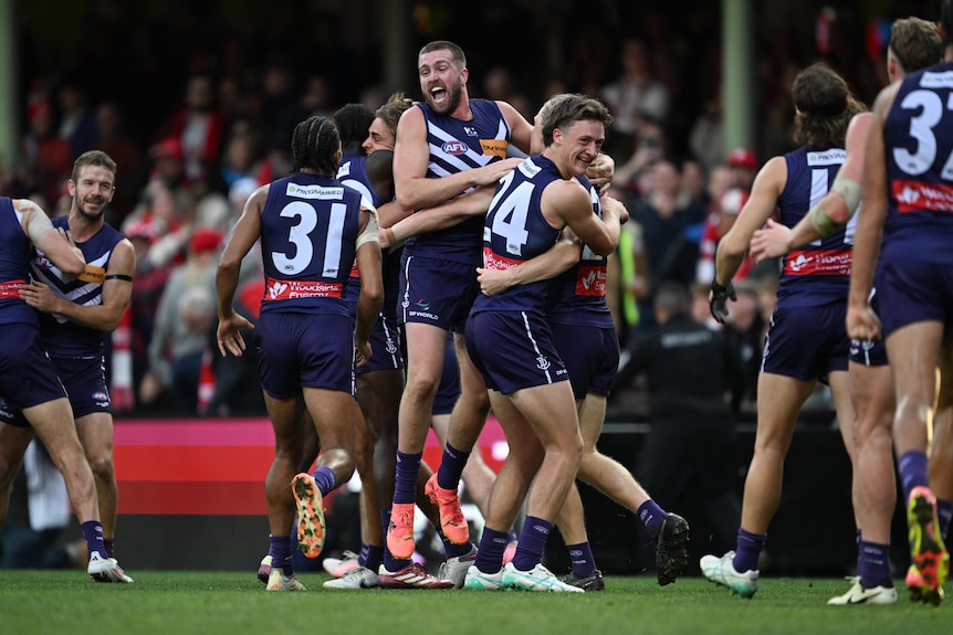 A group of Fremantle Dockers AFL players come together and embrace in celebration after a win. 