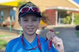 A young boy holds up a broze medal