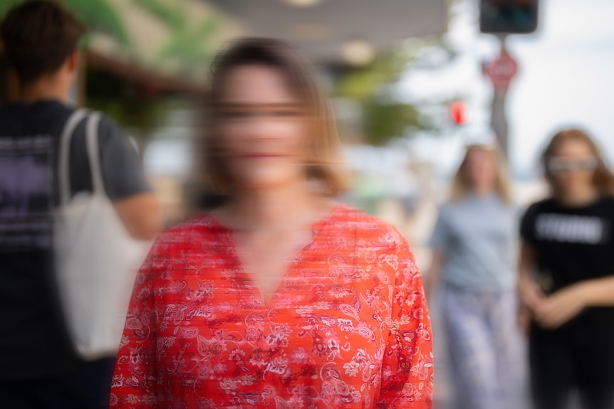 An unidentifiable woman in a red shirt stands outside in a crowd of people