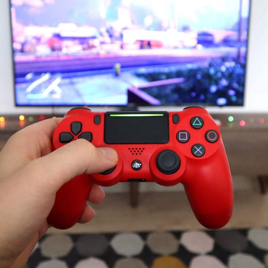Gaming controller in foreground, with game on tv in background.