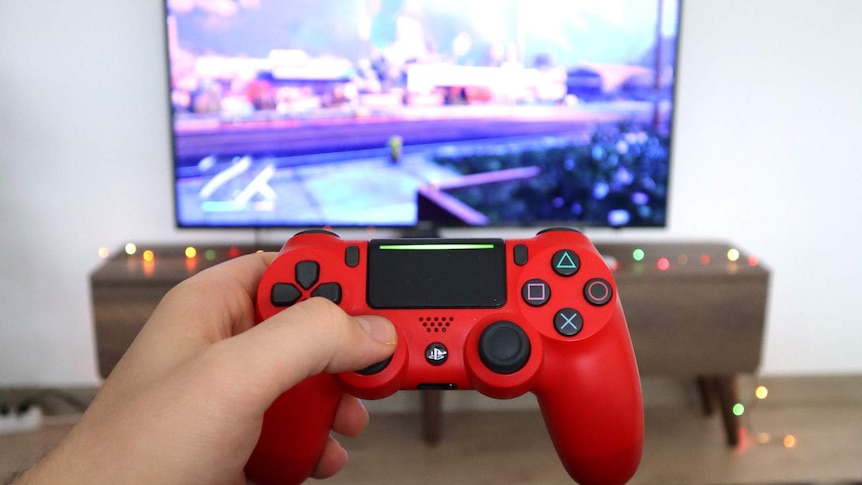 Gaming controller in foreground, with game on tv in background.