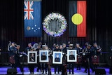 Police officers on stage at a memorial service holding four portraits of killed officers.