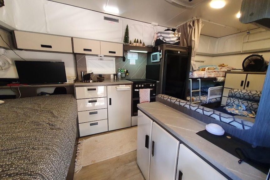 The interior of a family's caravan, showing beds, a TV and a kitchenette.