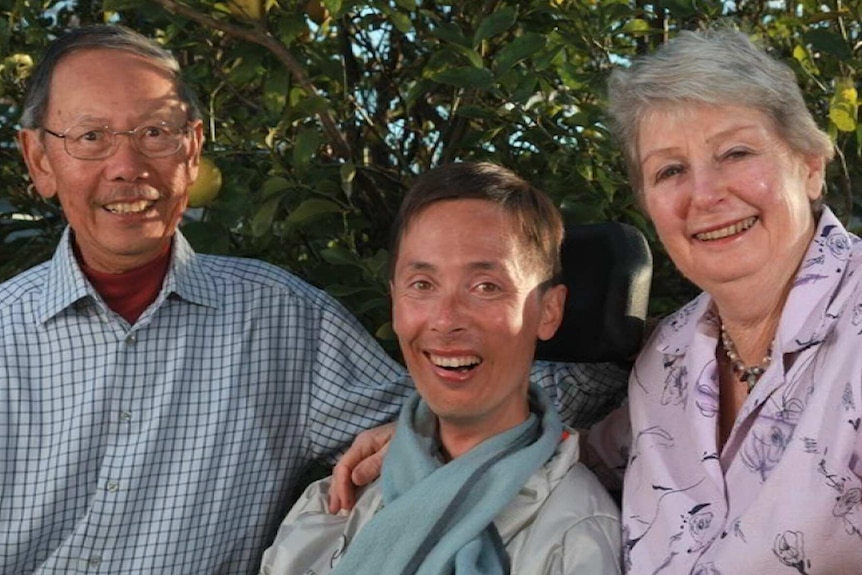 Michael Lee, sitting in his wheelchair, poses for a photo with his father (l) and mother (r)