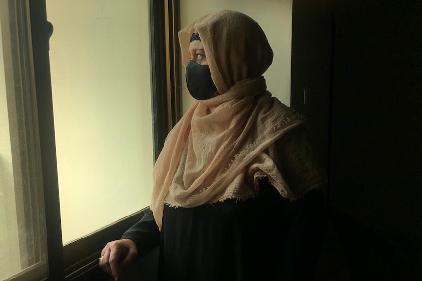 A woman wearing a head covering looks out a window.
