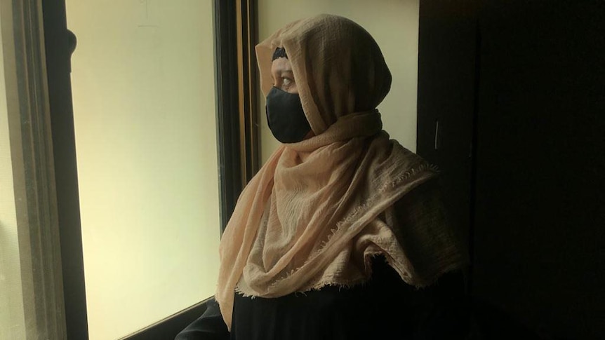 A woman wearing a head covering looks out a window.