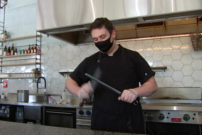 A man wearing black sharpens a knife in a commercial kitchen