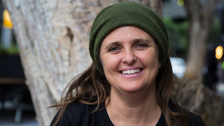 Quaker and environmental activist Lisa Wriley wears a green beanie and stands in front of a tree.